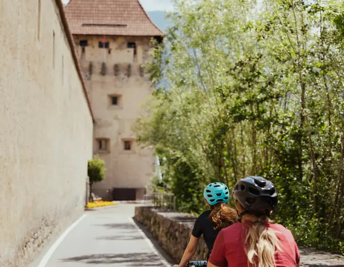 Radfahrerinnen auf dem Radweg an einer historischen Stadtmauer im Vinschgau