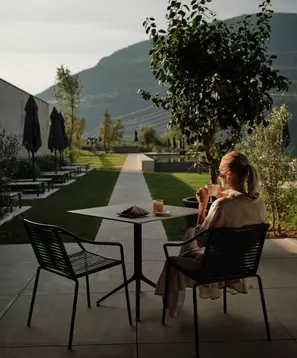 Frau mit Getränk auf der Terrasse mit Blick über Liegewiese und Berge